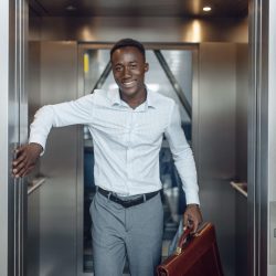 Black businessman goes into the elevator in office building. Successful business person, black man in formal wear, shopping center